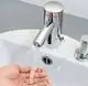 Ein verchromter Wasserhahn mit Sensorsteuerung von CLAGE, der Wasser in eine Hand ausströmt, montiert auf einem weißen Waschbecken.